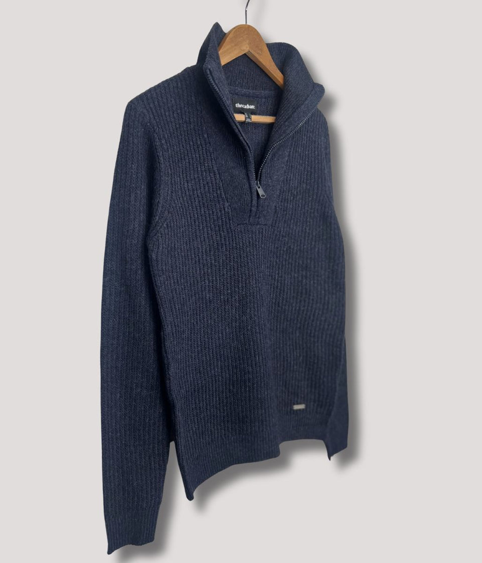 Navy blue sweater 1/4 zip on a wooden hanger against a light gray background