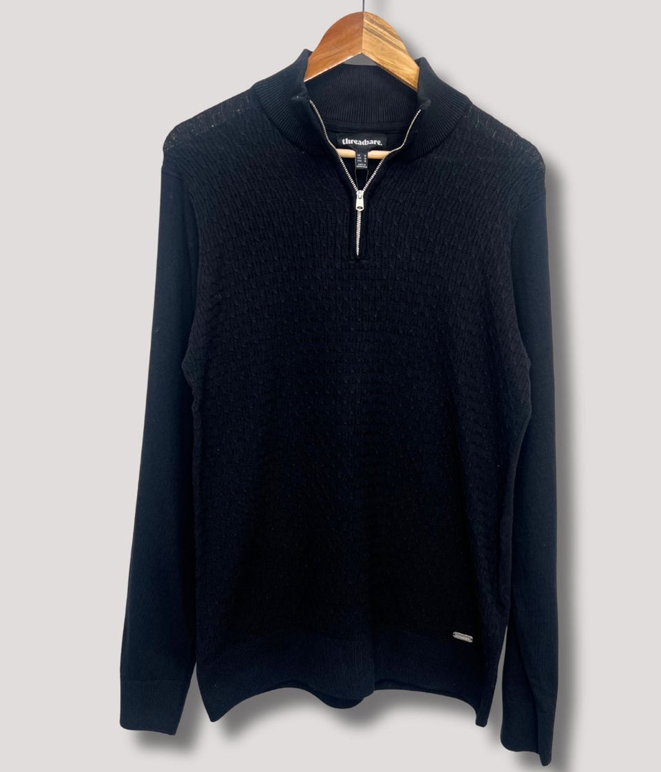 Black sweater with a zipper on a wooden hanger against a light gray background