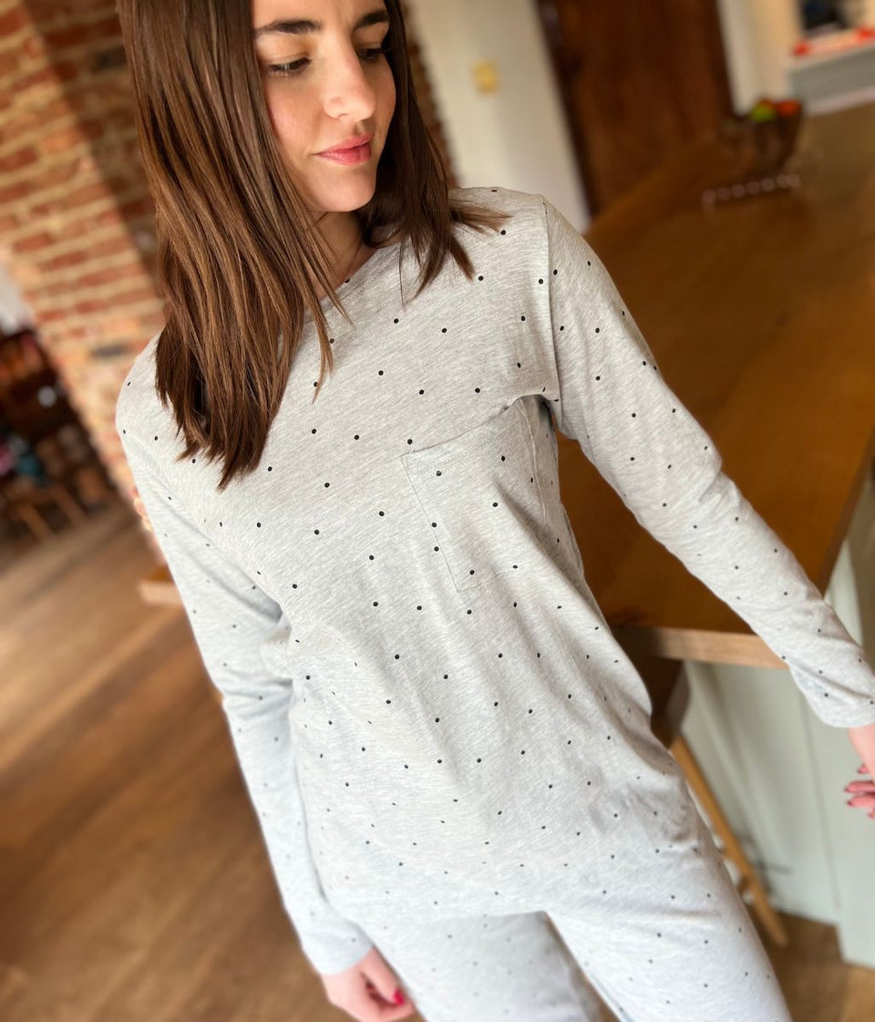 Woman wearing a light gray long-sleeve top with black polka dots indoors.