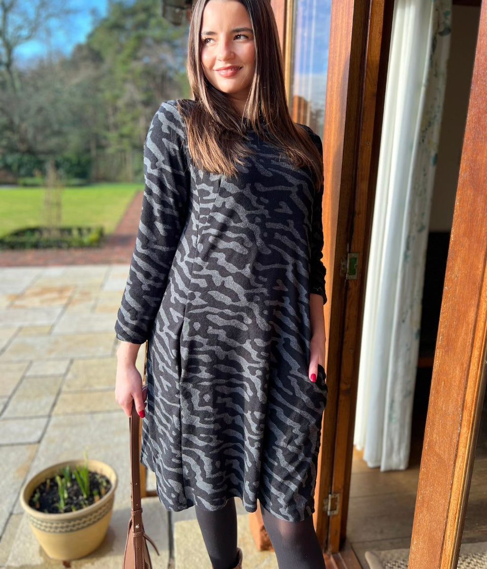 Woman wearing a patterned dress standing in a doorway with a garden view.