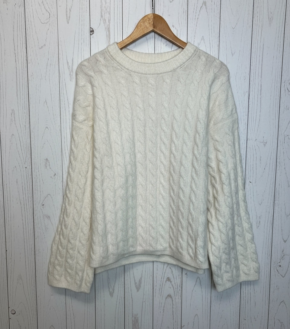 White cable knit sweater on a wooden hanger against a white background
