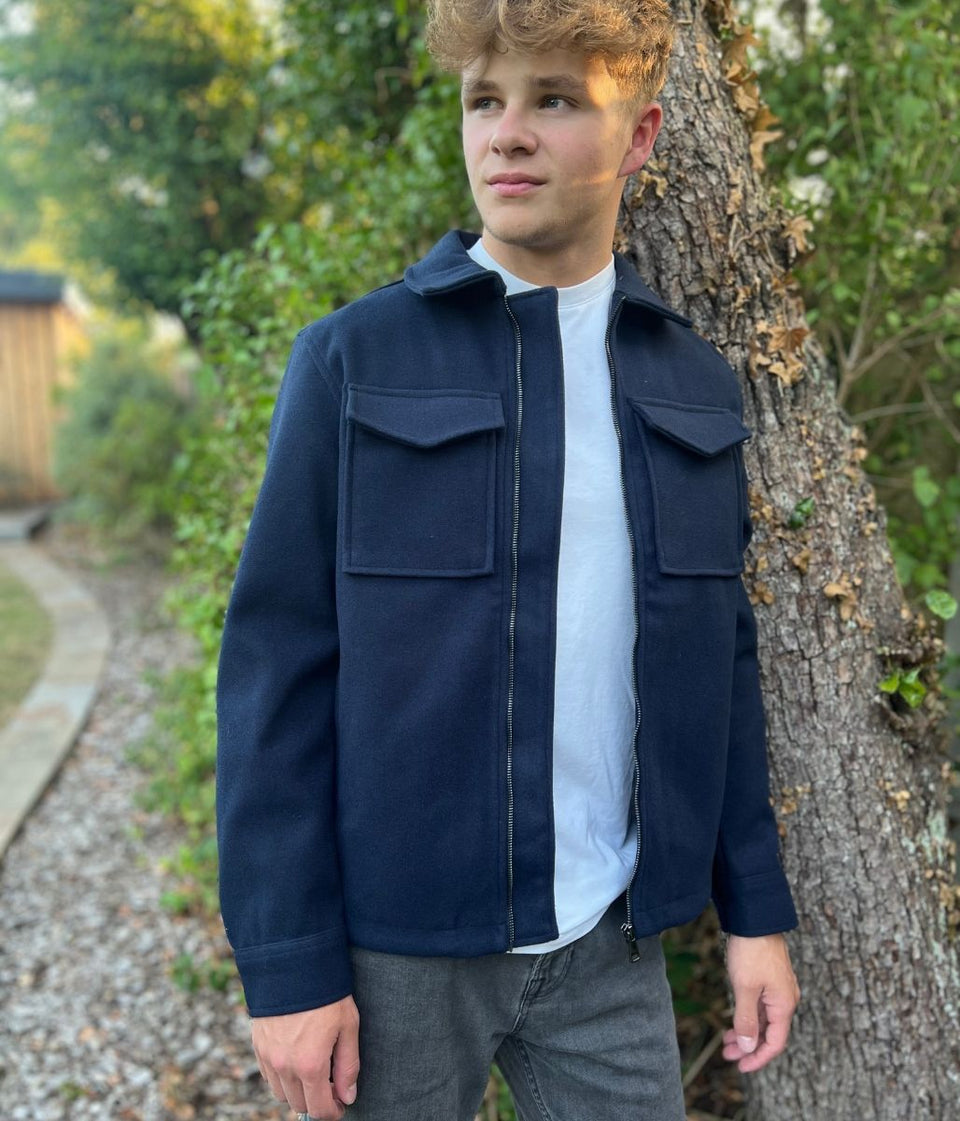 Man wearing a navy jacket standing next to a tree