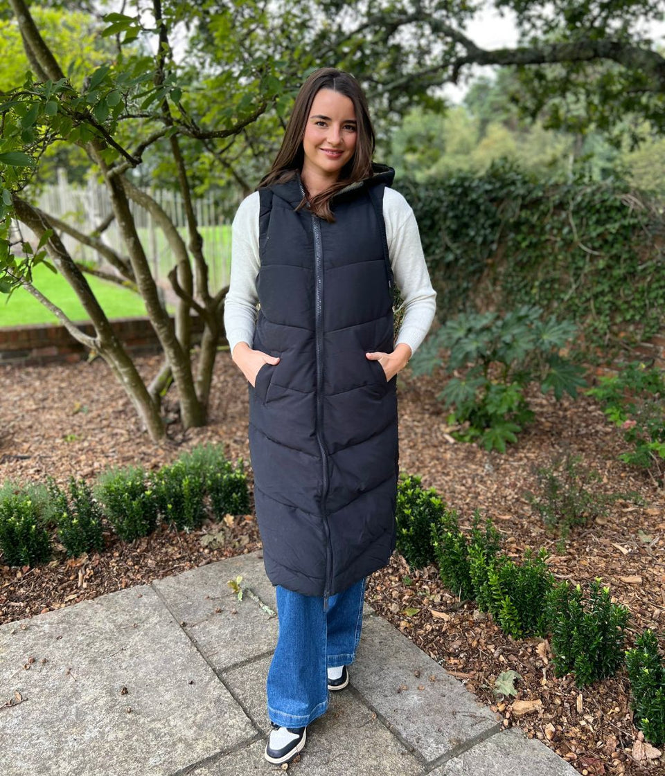 Person wearing a long puffer vest outdoors in a garden setting