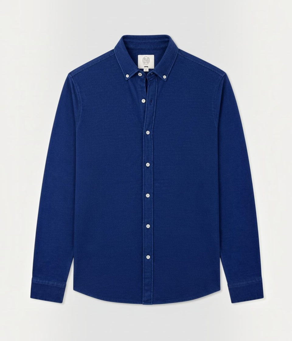 A long-sleeve button-down shirt in a deep royal blue color, featuring a classic pointed collar with two silver-tone metal buttons and a matching button-down front. The shirt is displayed flat against a clean, light off-white background.
