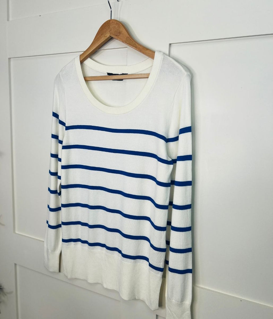 White sweater with blue stripes on a wooden hanger against a white wall